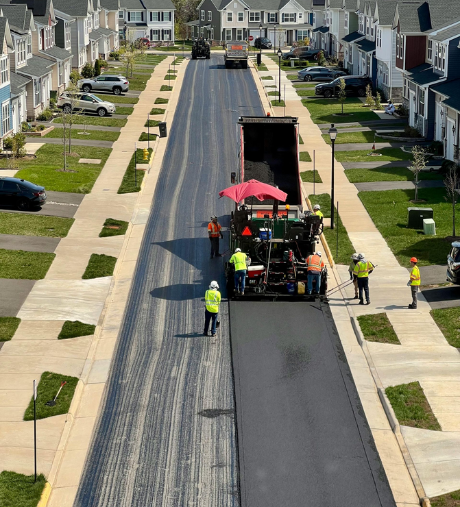 Construction crew paving a residential street with heavy machinery and materials in a neighborhood.