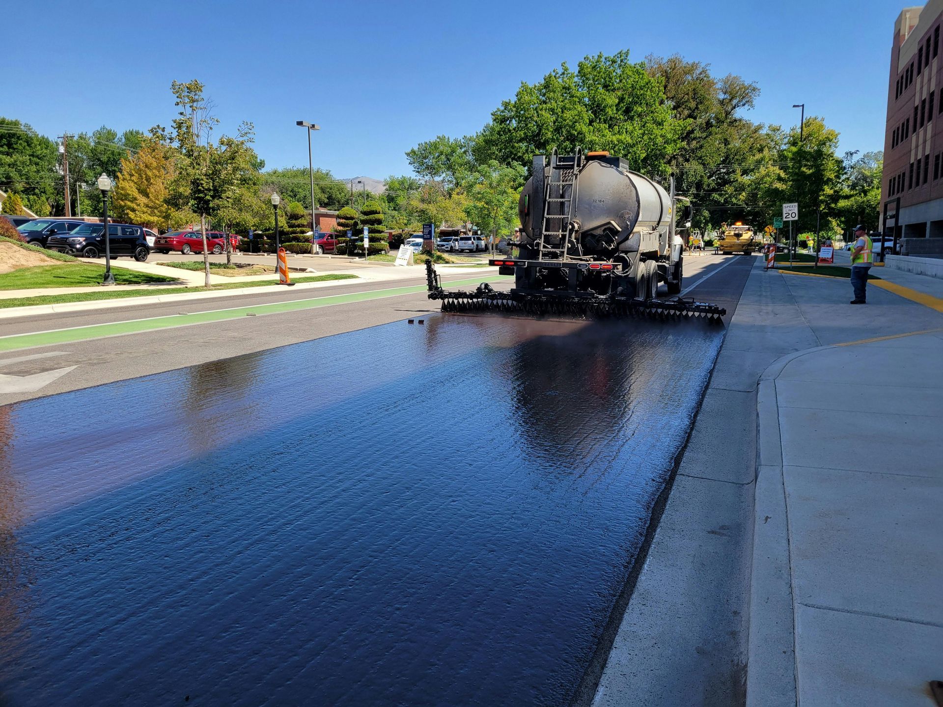 A truck applies a dark, liquid asphalt sealcoat to a residential street during a road maintenance project.