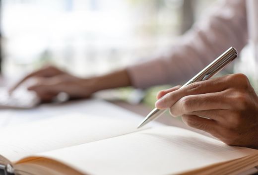 A person is writing in a notebook with a pen.