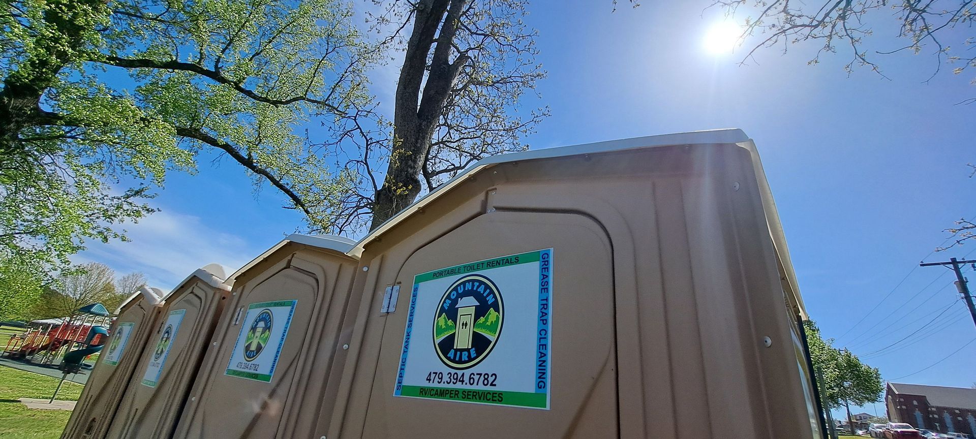 A row of portable toilets are sitting next to each other in a park.