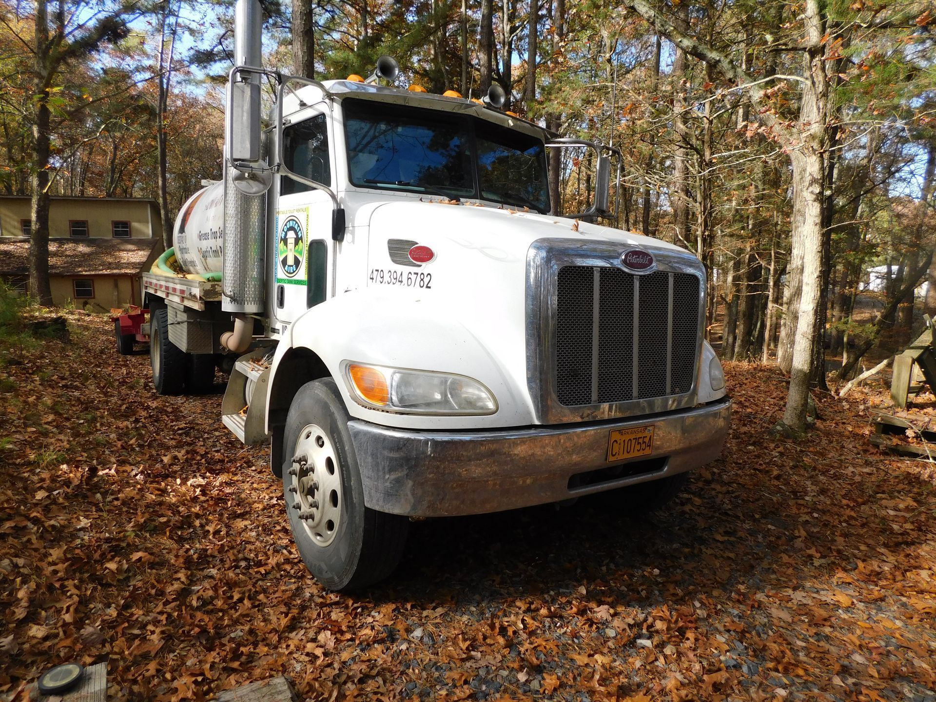 A white truck is parked in a pile of leaves in the woods.