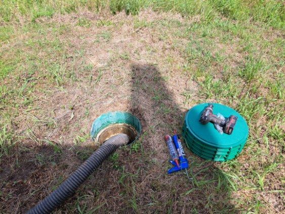 A hose is connected to a green container in the grass.