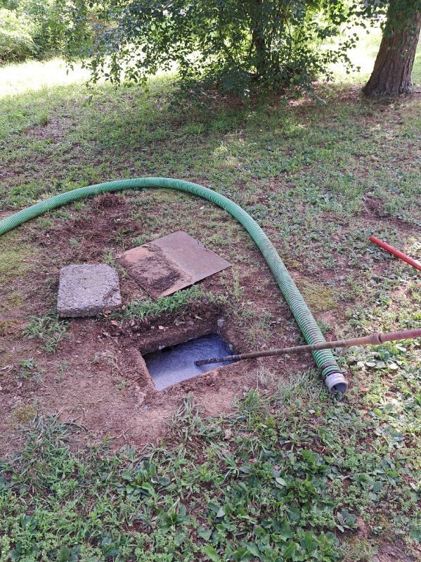 A green hose is connected to a hole in the ground.