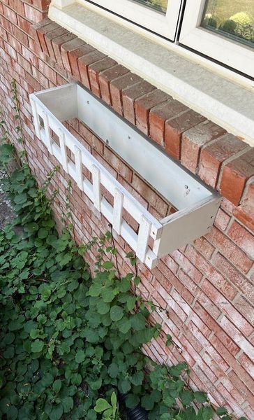 A white planter is sitting on a brick wall next to a window.