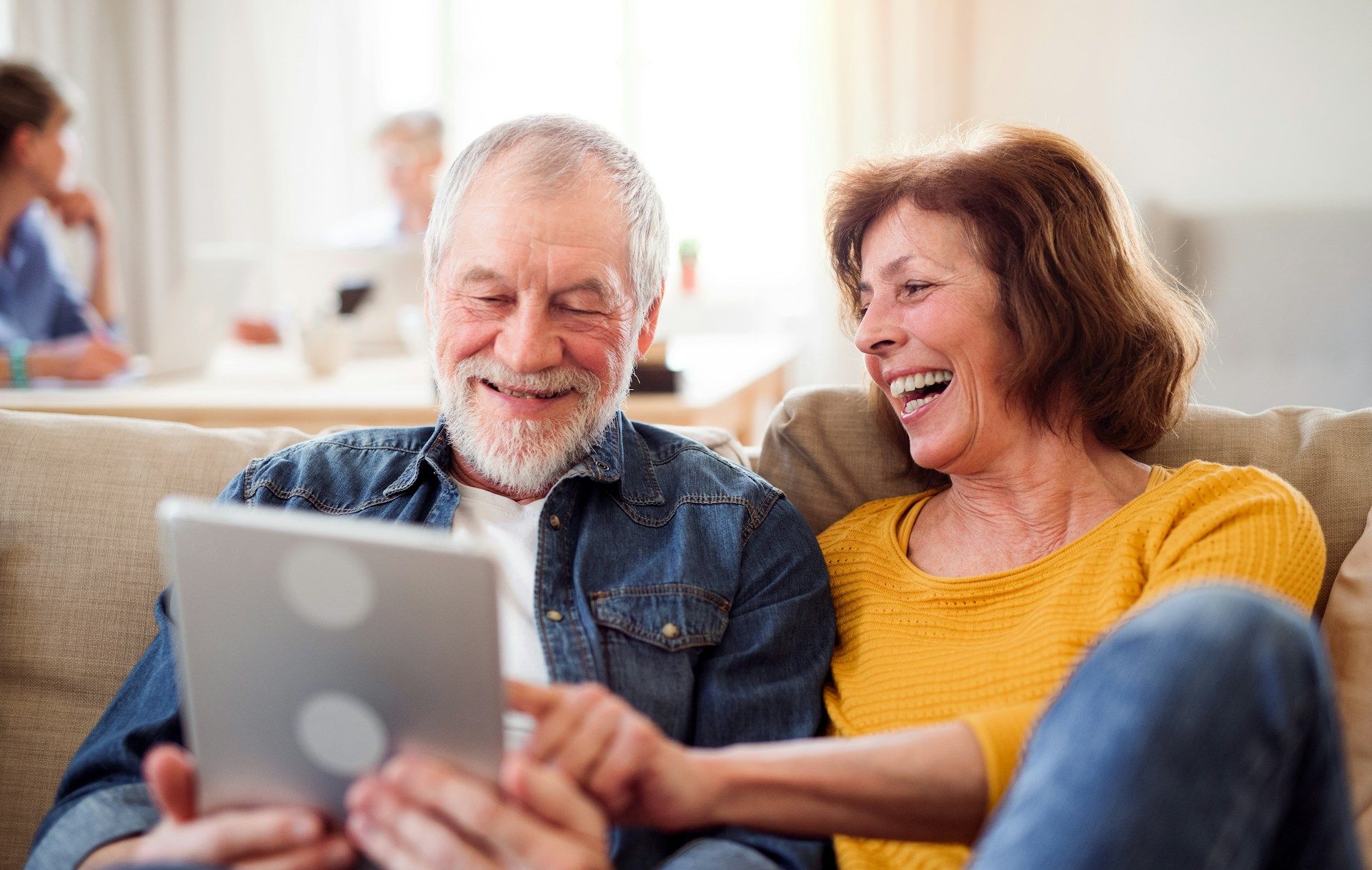 An elderly couple is sitting on a couch looking at a laptop computer.