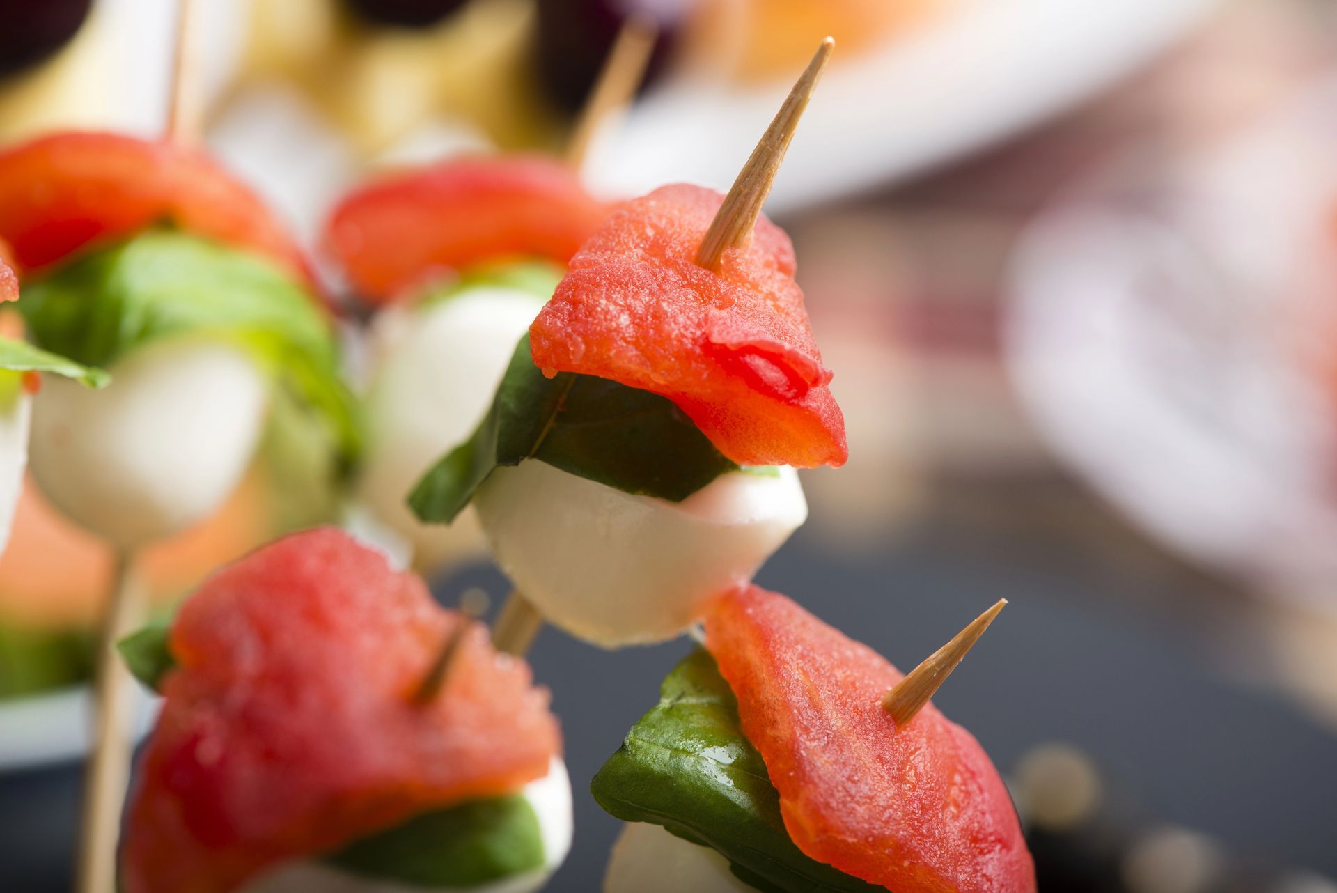 Spiedini caprese: palline di pomodoro, basilico e mozzarella infilzate con stuzzicadenti.