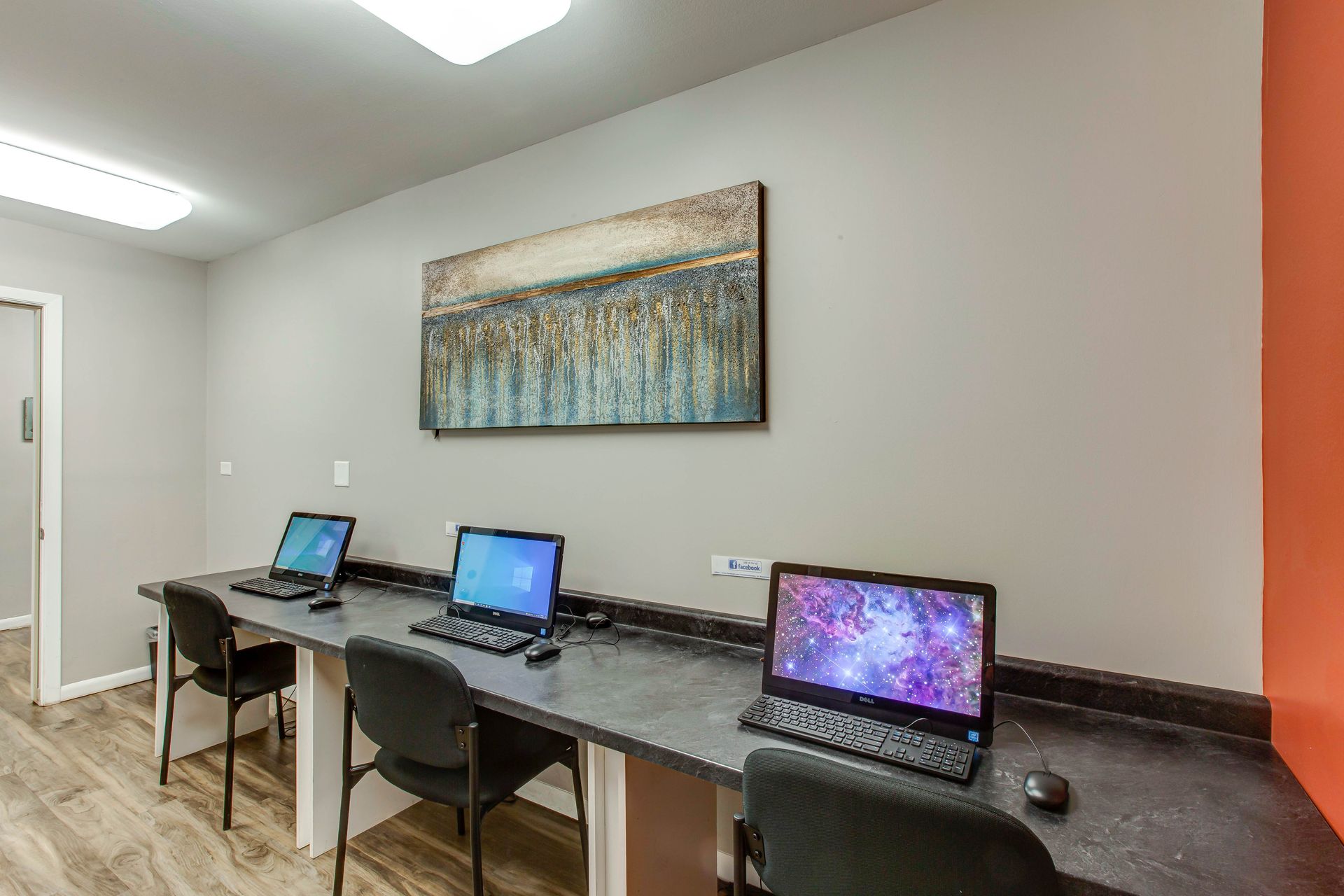 Shared study space with three laptops on a long desk and wall art above.