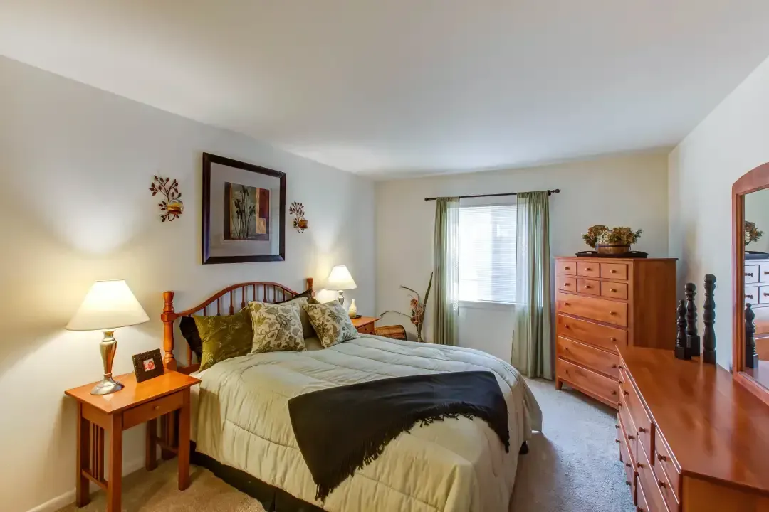 Cozy bedroom with a bed, dresser, desk, lamp, and window with sheer curtains