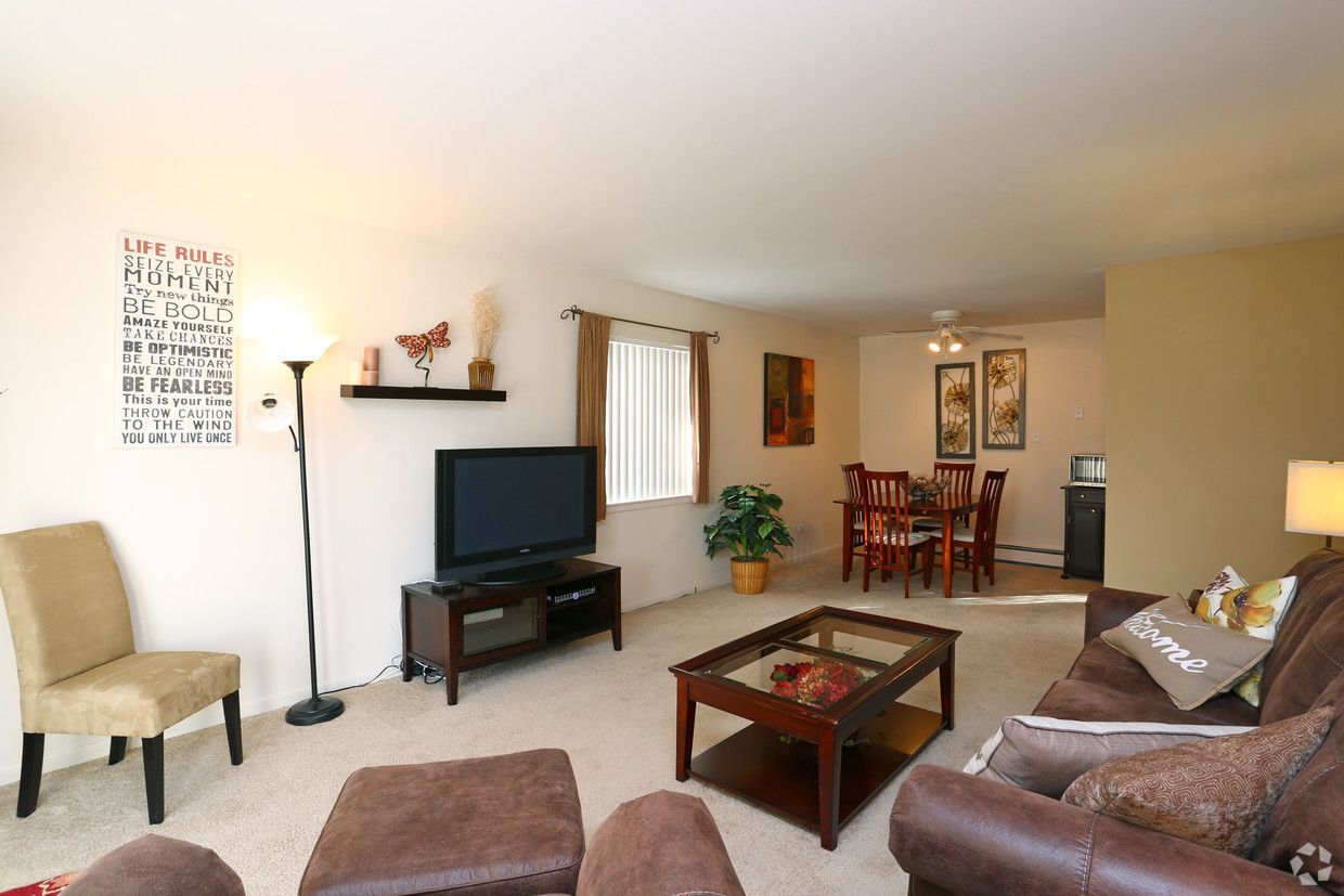 Bright living room with brown sofas, TV on stand, coffee table, and dining area in the back