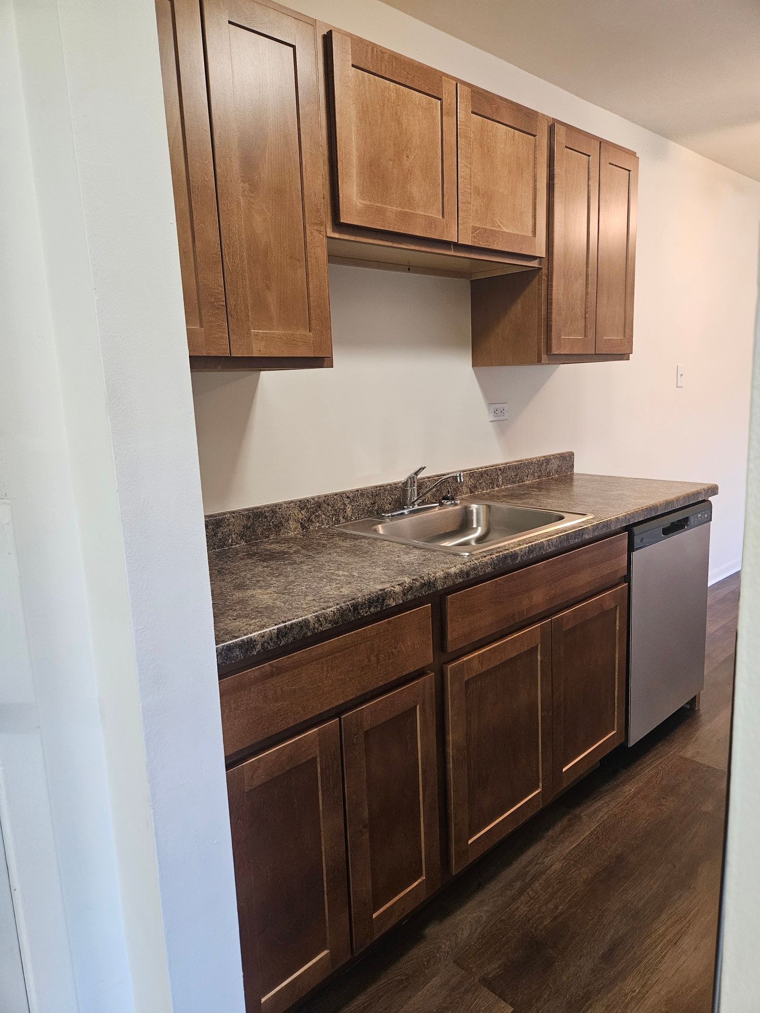 Empty kitchen alcove with wood cabinets, granite countertop, sink, and stainless dishwasher