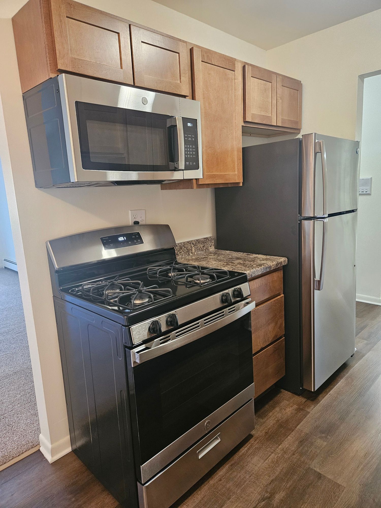 Modern kitchen with stainless steel stove, microwave, and refrigerator, wood cabinets, and granite countertops