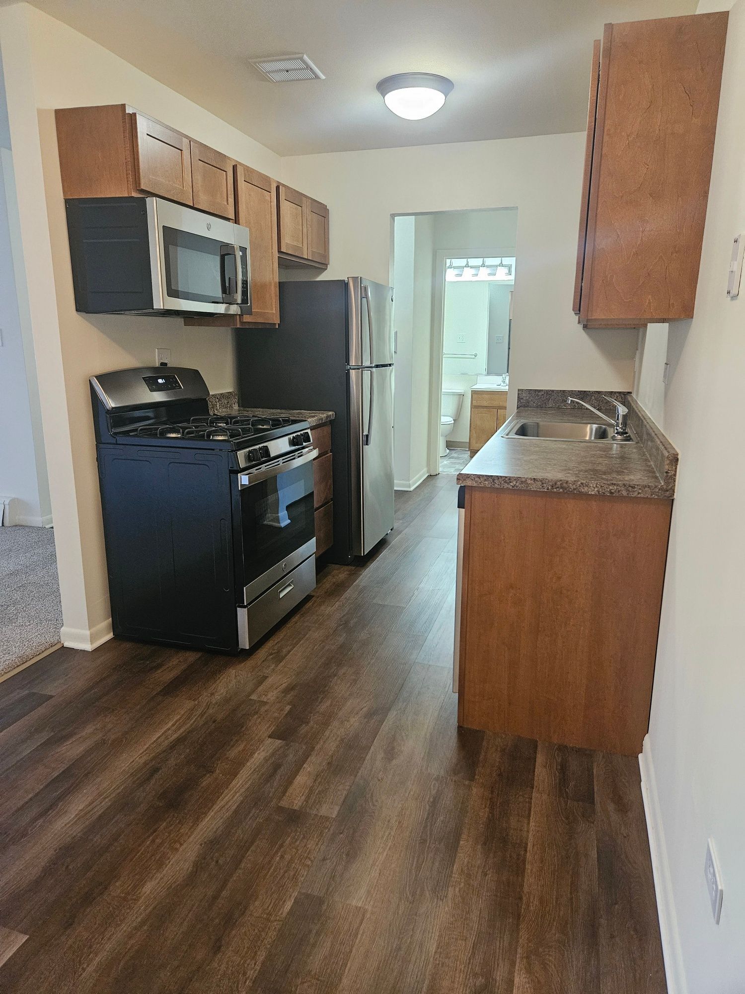 Compact galley kitchen with dark wood cabinets, black stove, stainless fridge, and wood floor