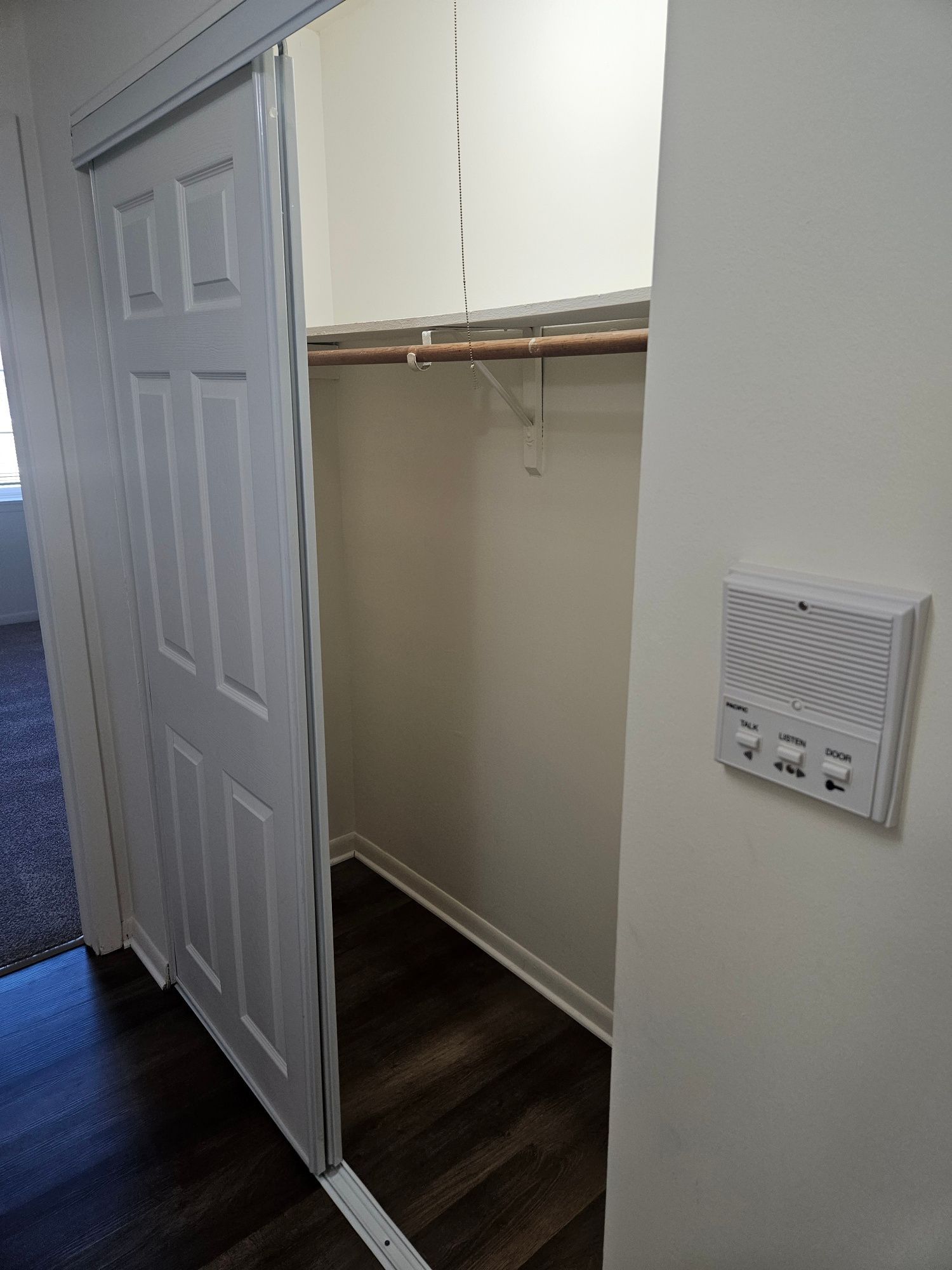 Open closet with sliding mirrored door, white shelves, hanging rod, and dark wood floor.
