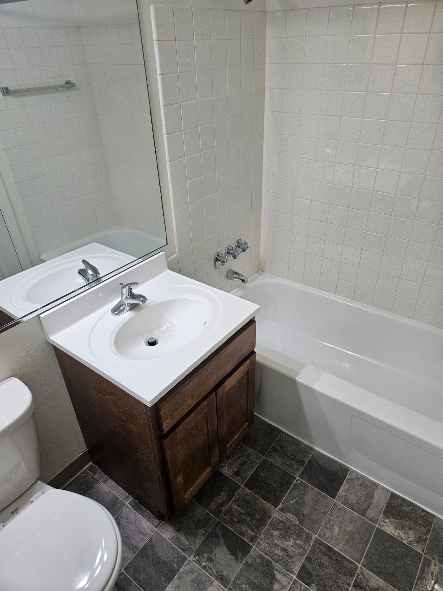 Small bathroom with white sink vanity, toilet, tiled floor, mirror, and bathtub.