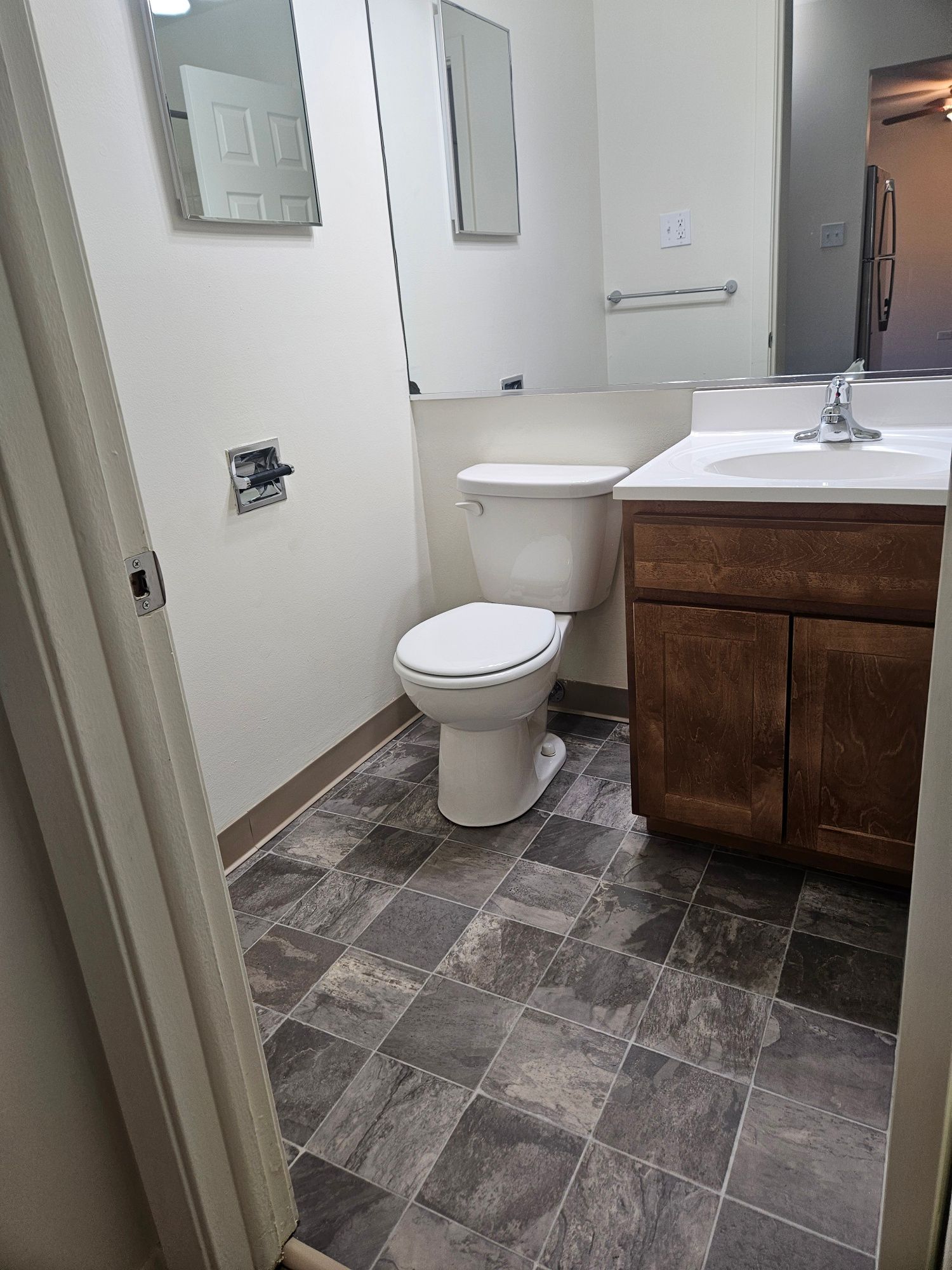 Small bathroom with toilet, sink vanity, mirror, and gray patterned floor tiles.