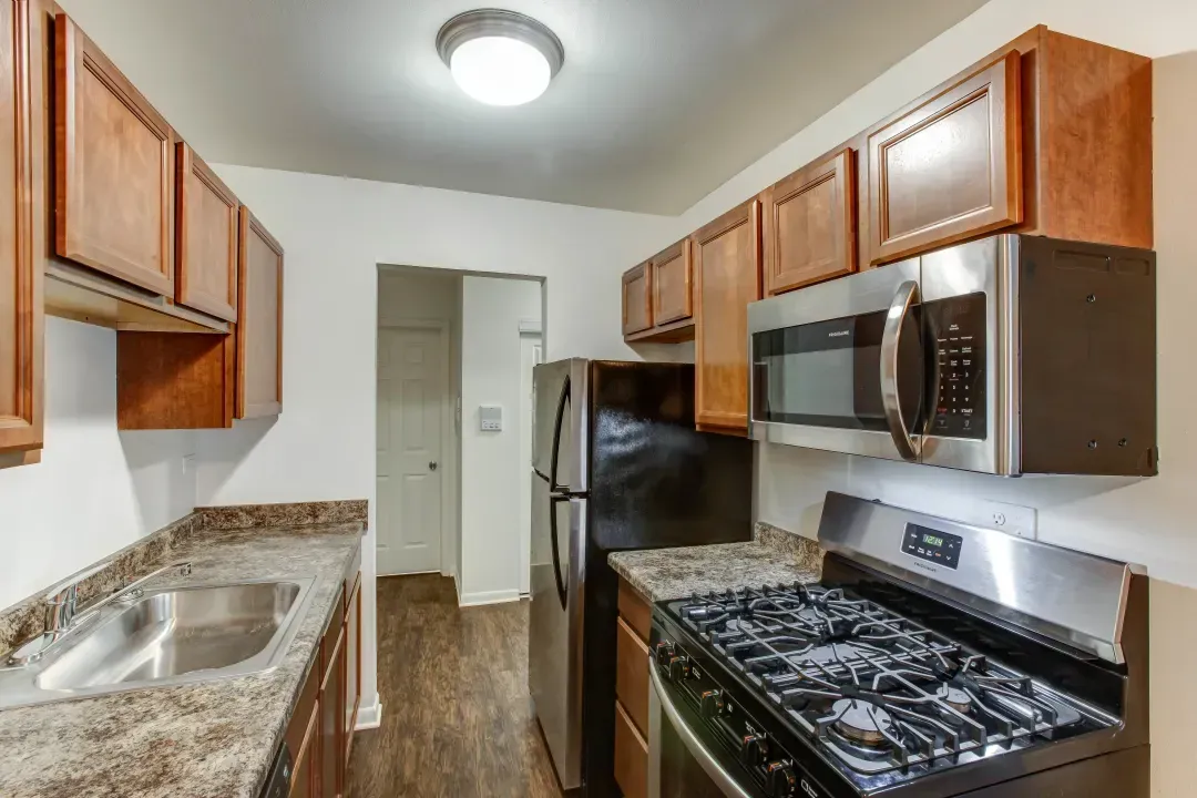 Narrow kitchen with wooden cabinets, granite counters, black appliances, and a stainless sink.