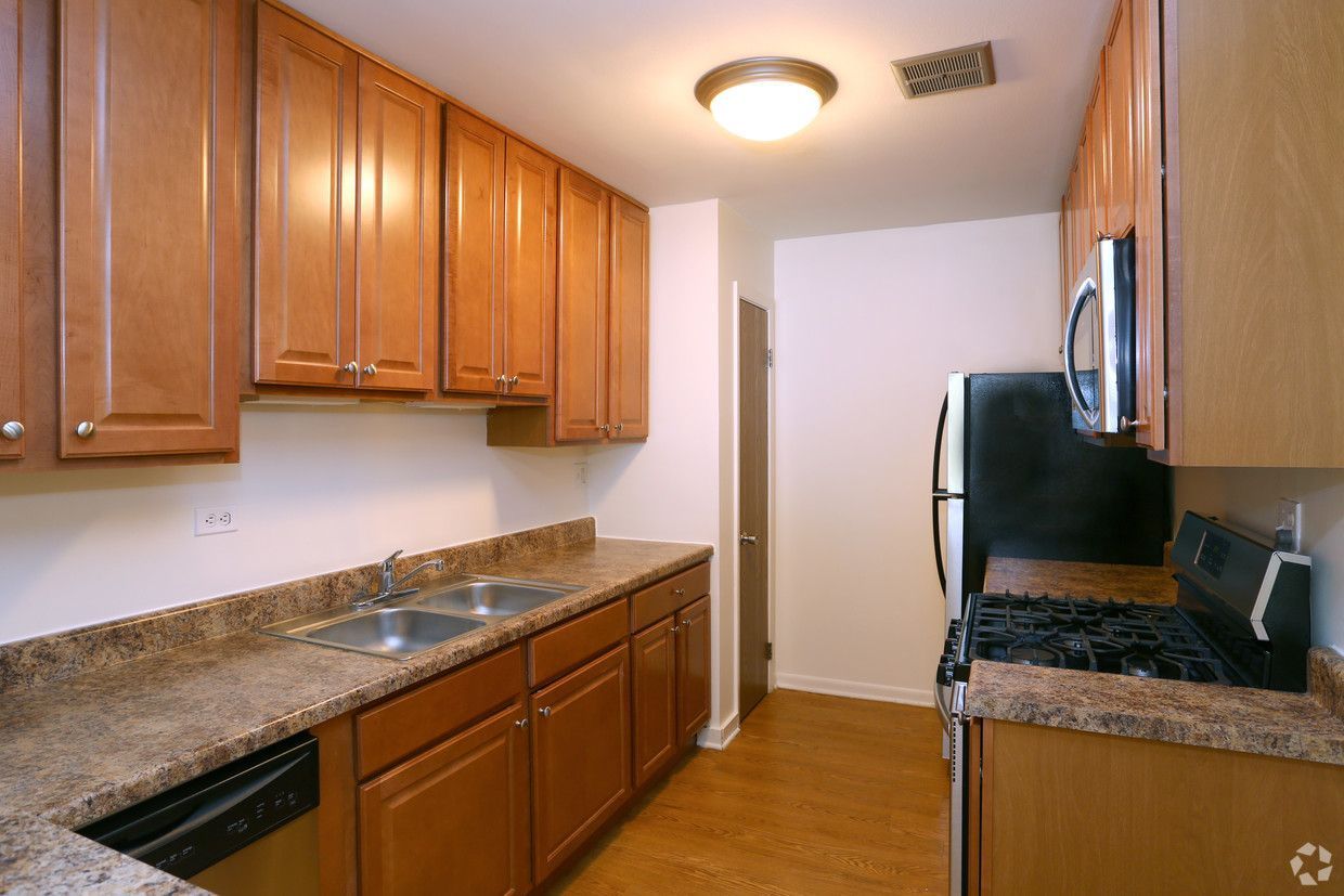 Narrow kitchen with wood cabinets, granite counters, black appliances, and a ceiling light.