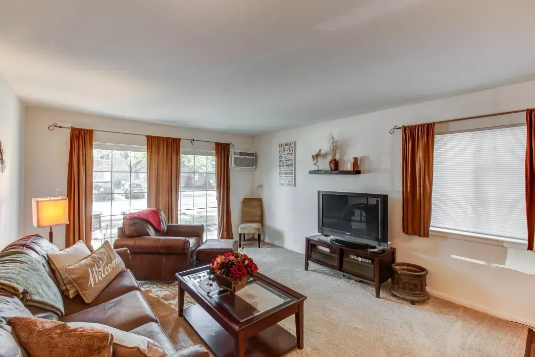 Bright living room with tan sofa, coffee table, TV, and orange curtains by a window