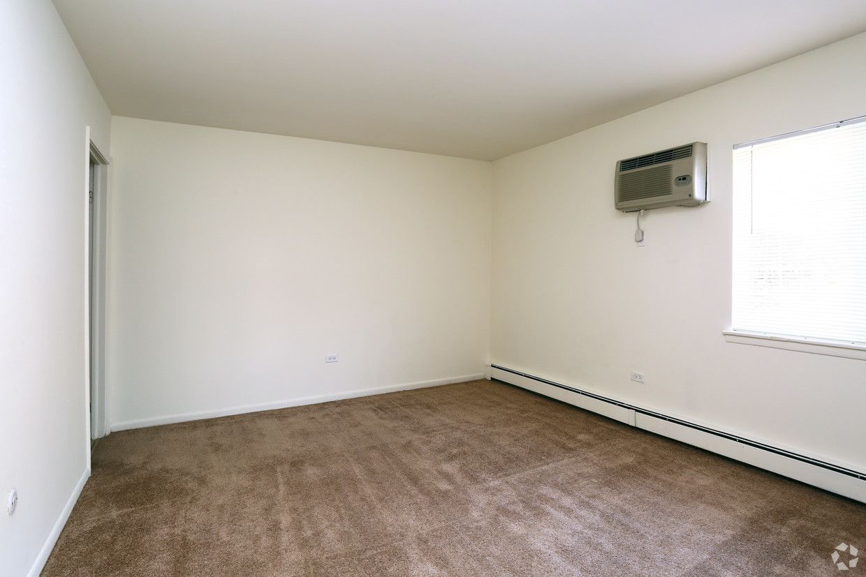 Empty beige room with brown carpet, window air conditioner, and bright window blinds.