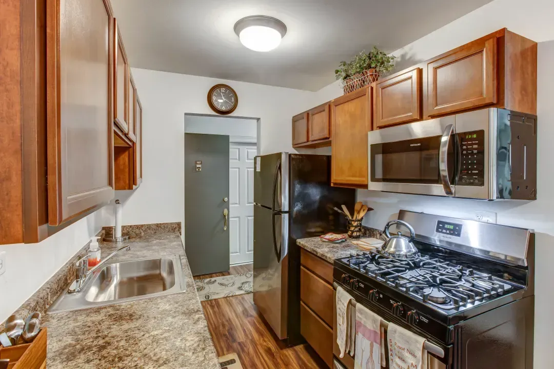 Galley kitchen with wood cabinets, granite counters, stainless appliances, and a gas stove
