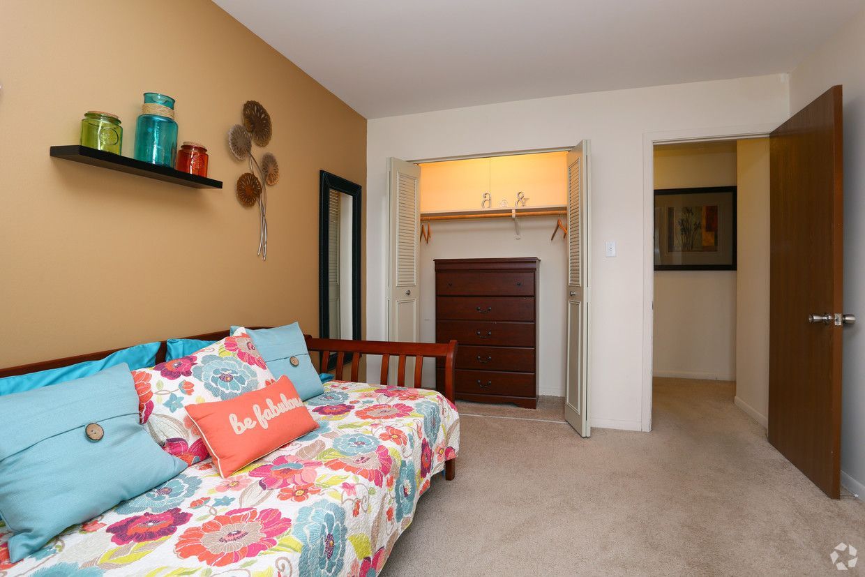 Bedroom with floral daybed, tan walls, dresser in alcove, and open closet door