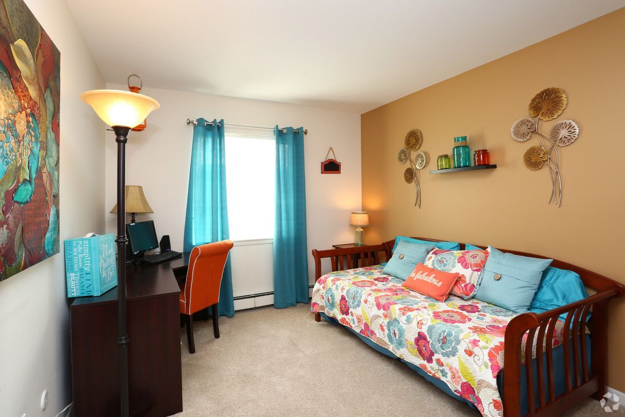 Colorful bedroom with twin bed, desk, blue curtains, floor lamp, and wall art