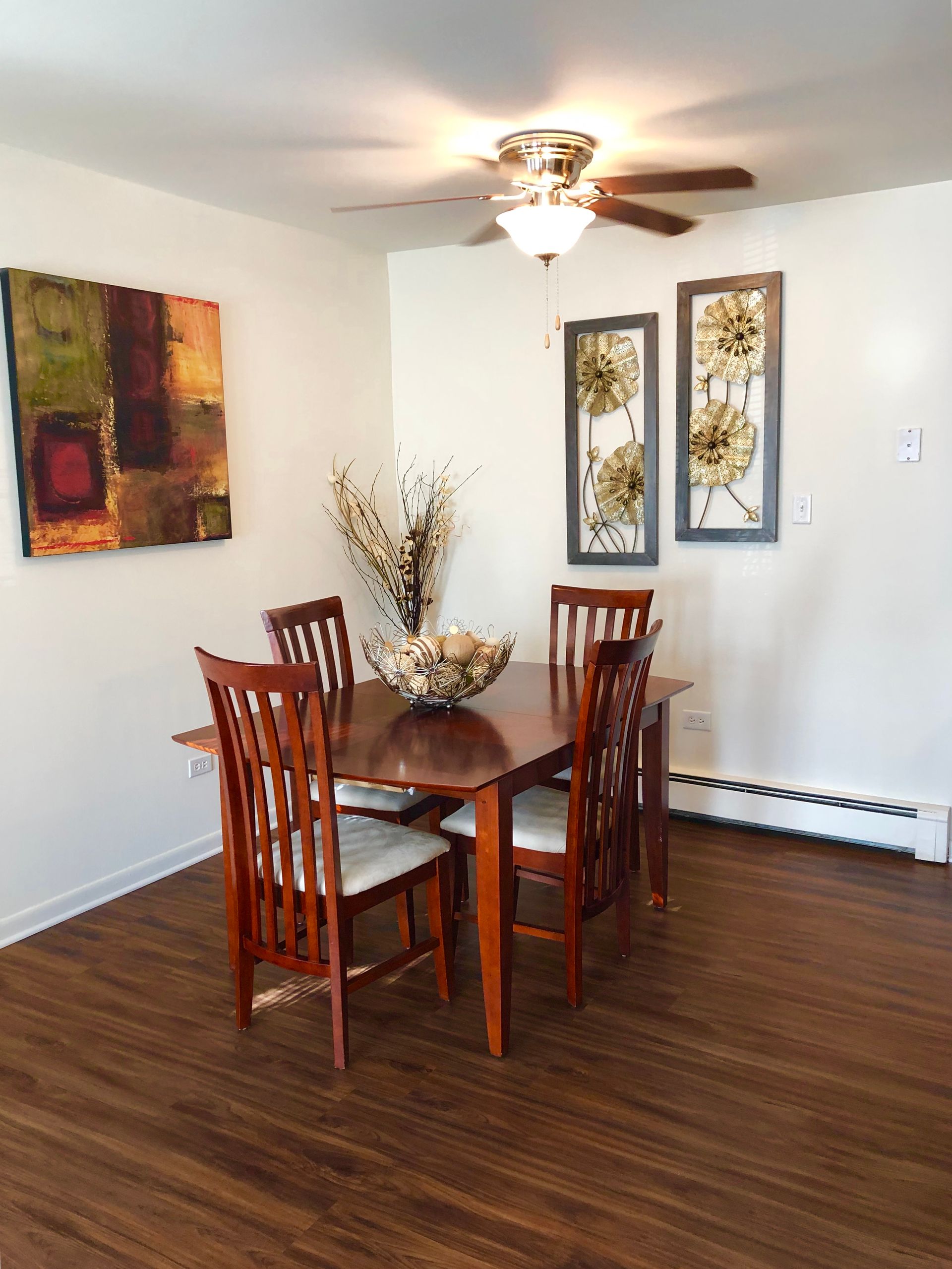 Dining room with wooden table and chairs, wall art, and a ceiling fan on a hardwood floor.