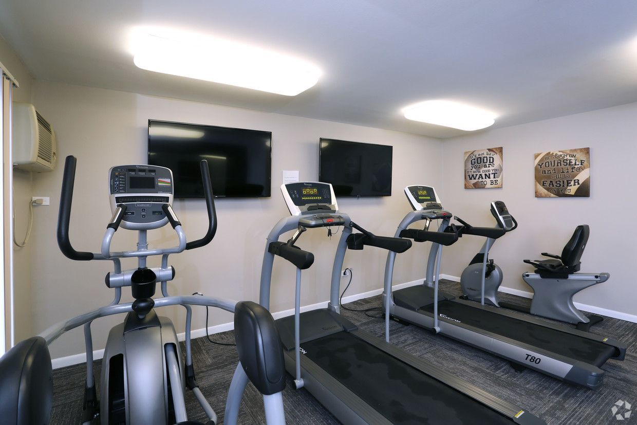Gym room with several treadmills and exercise bikes under wall-mounted TVs
