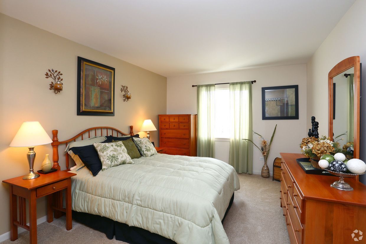 Bright bedroom with a bed, dresser, lamps, artwork, and a window with curtains