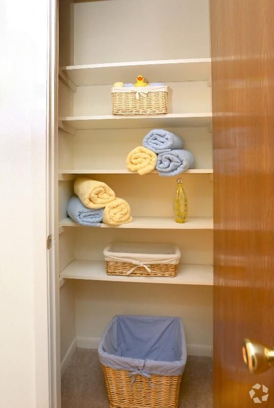 Bathroom linen closet with folded towels, baskets, and a laundry hamper on the bottom shelf