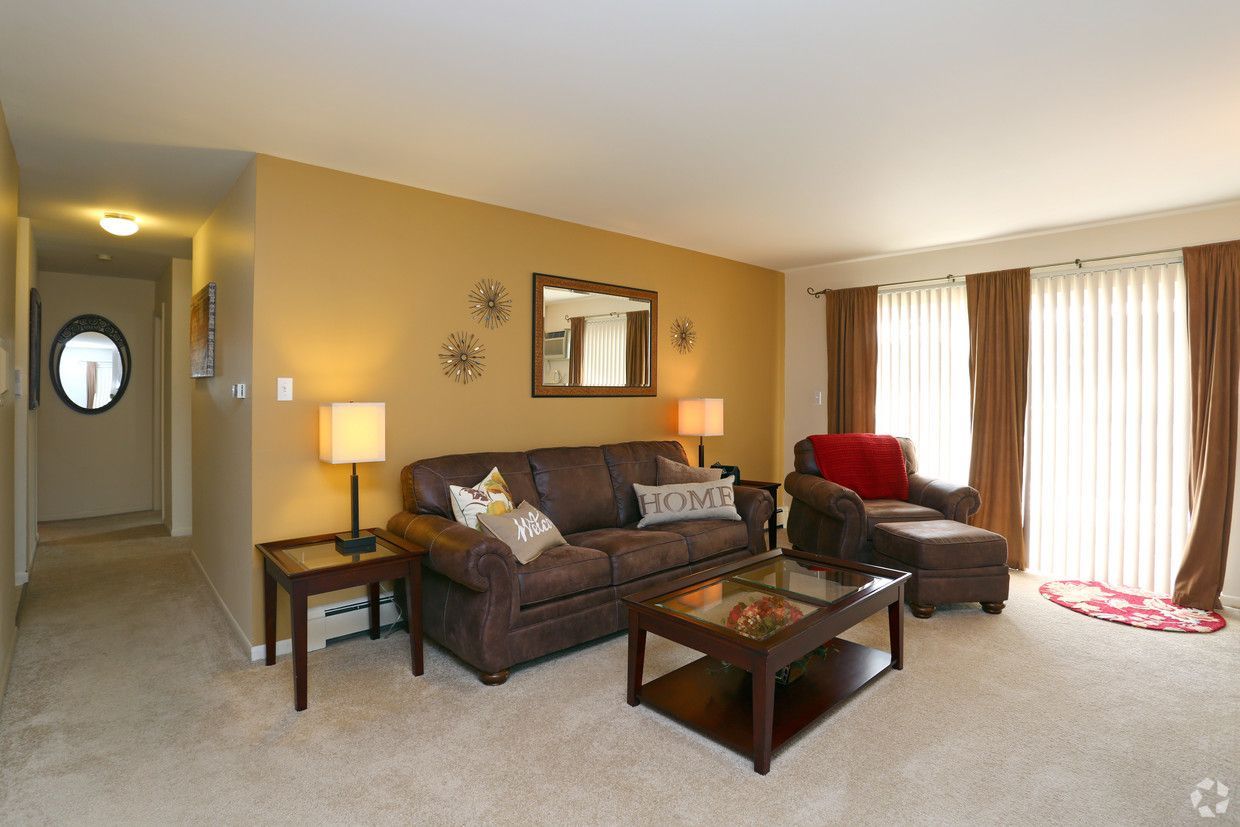 Living room with brown sofa, red chair, coffee table, lamps, and sliding glass doors with curtains.