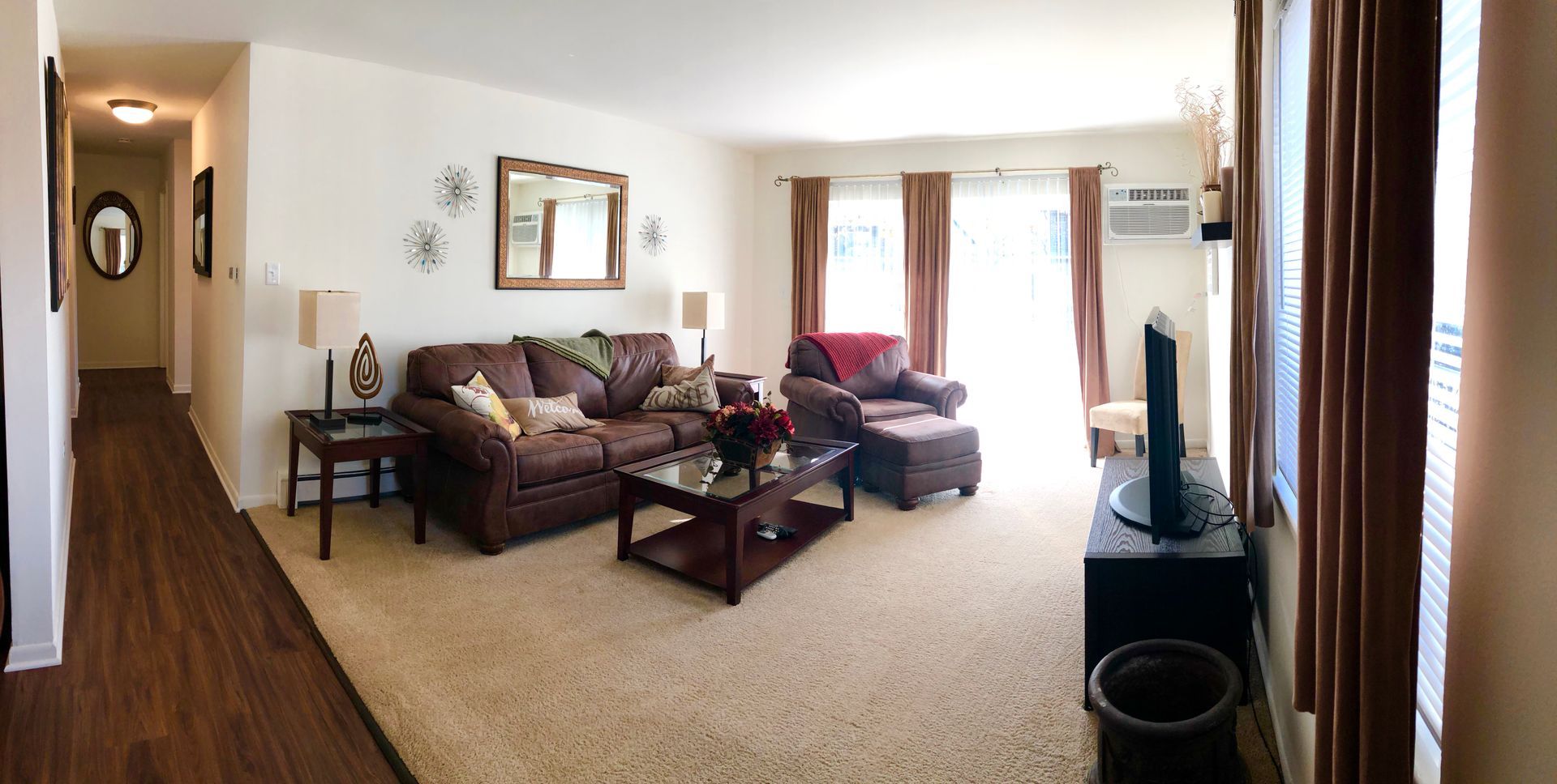 Living room with brown sofa, loveseat, coffee table, carpet, and tall windows with curtains