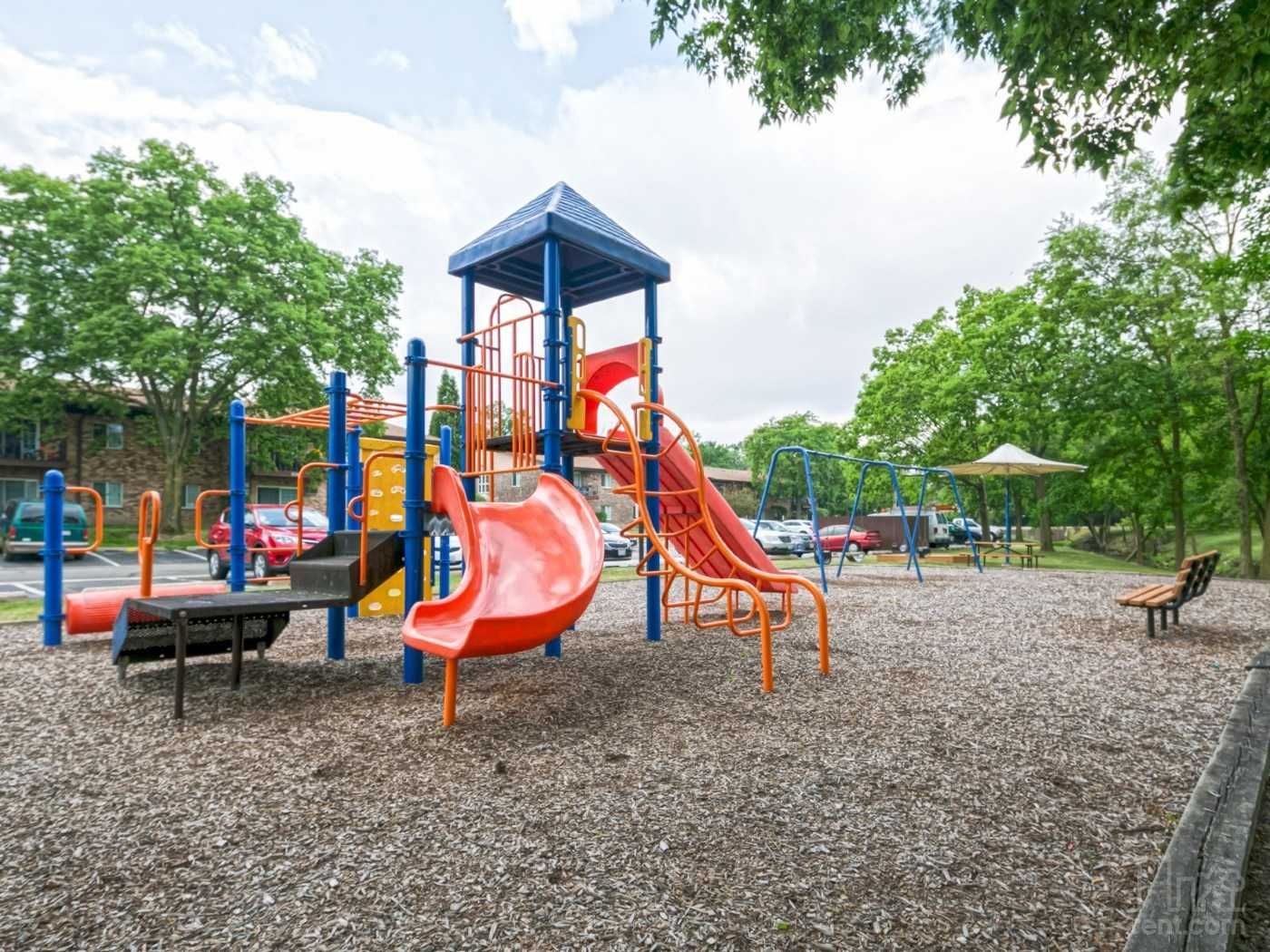 Colorful playground with slides, climbing structures, benches, and gravel ground in a park