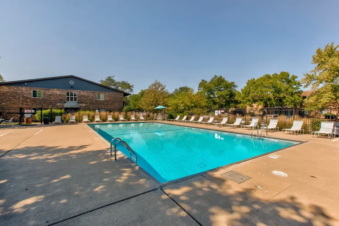 Outdoor swimming pool beside a brick building, with lounge chairs and trees on a sunny day