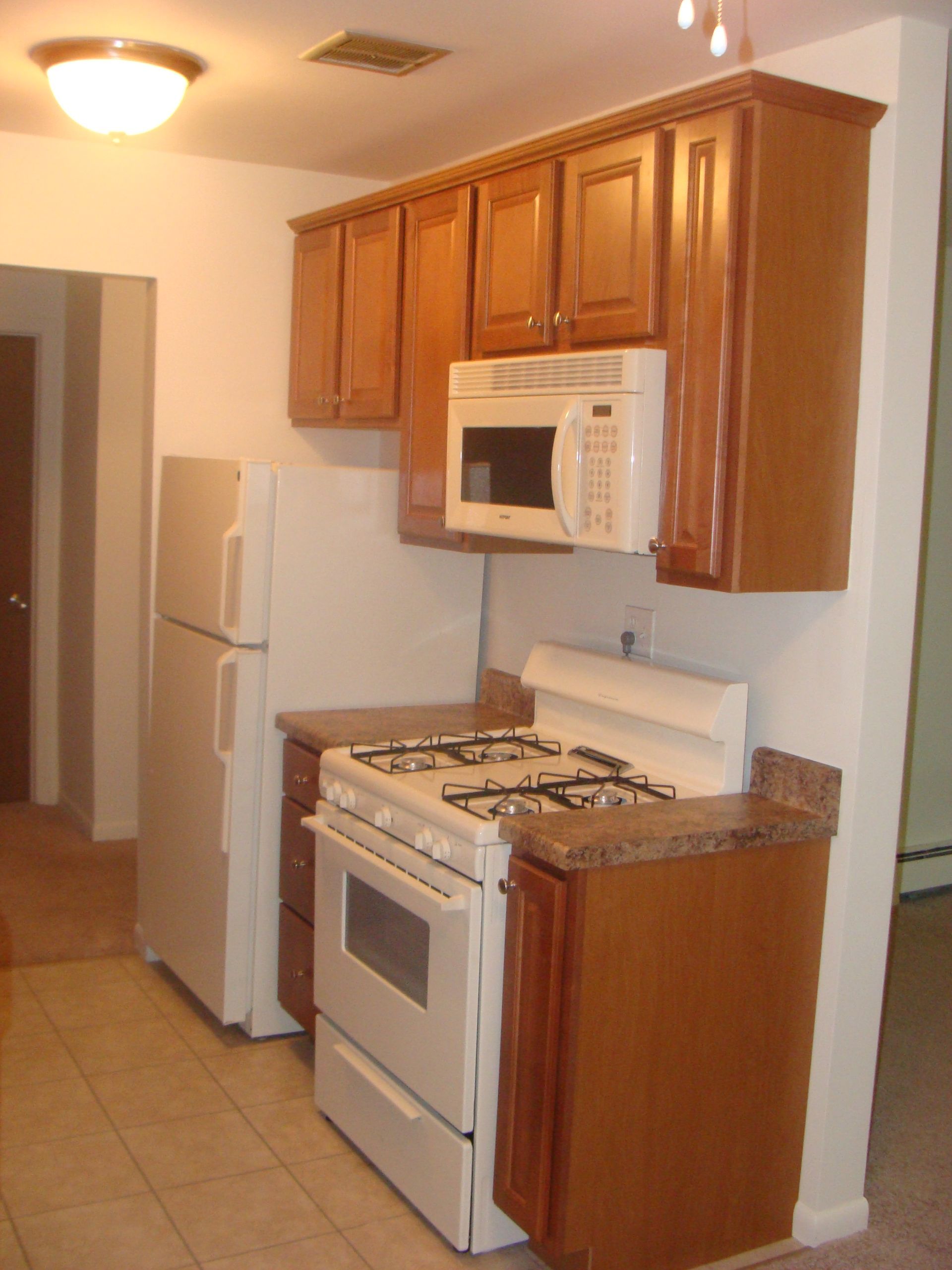 Small kitchen with wooden cabinets, white refrigerator, stove, microwave, and granite countertop.