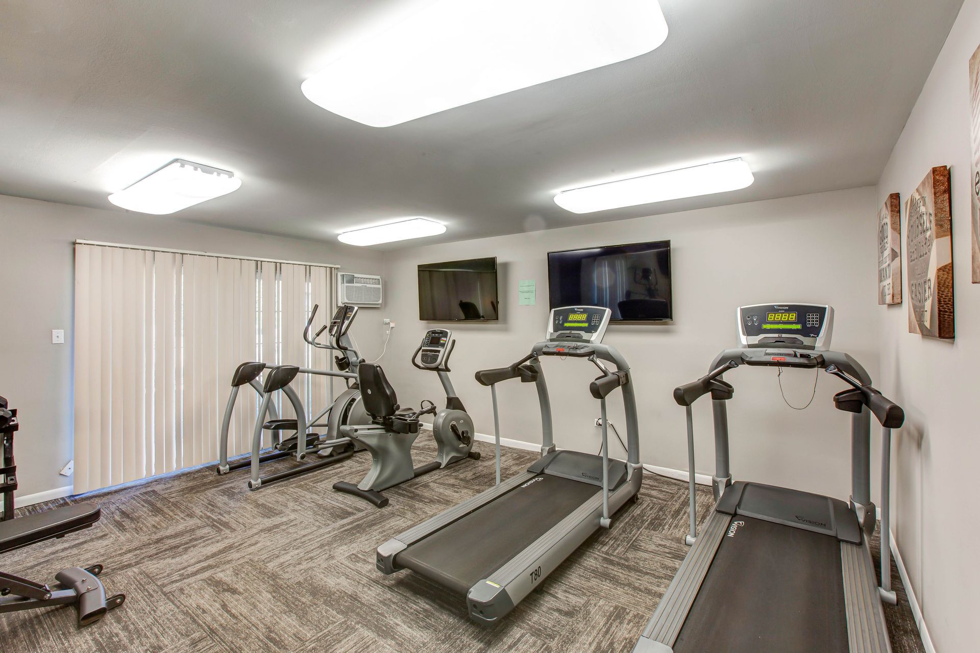 Small home gym with treadmills, ellipticals, wall-mounted TVs, and mirrored walls