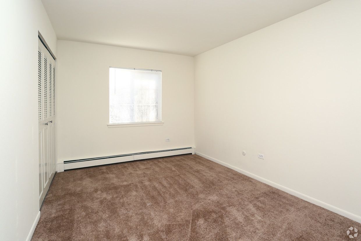 Empty beige bedroom with carpet, closet doors, and a window with blinds