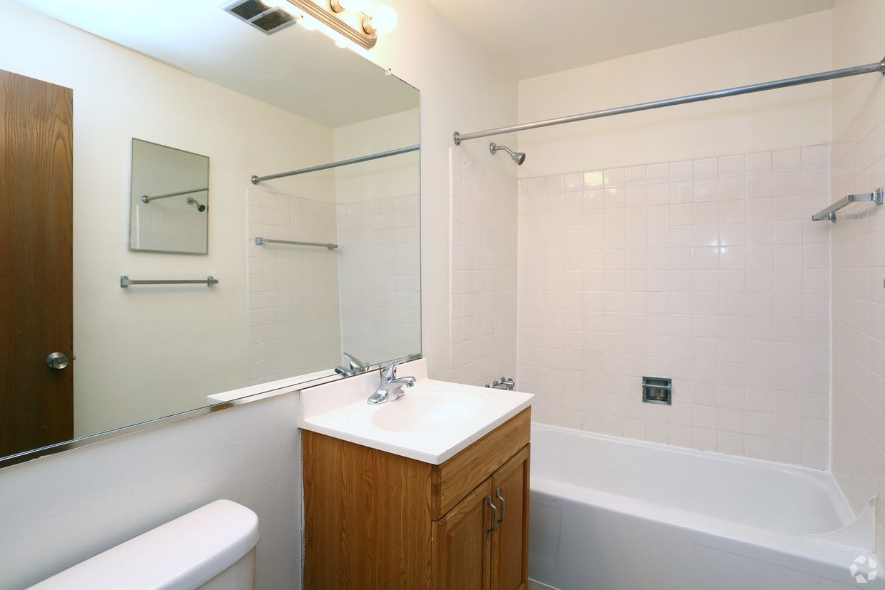 Bright bathroom with tub, toilet, vanity sink, mirror, and towel bar in white and wood tones