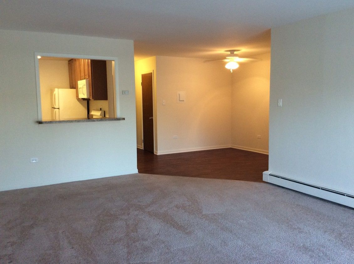Empty carpeted living room with pass-through to kitchen and warm-lit dining area