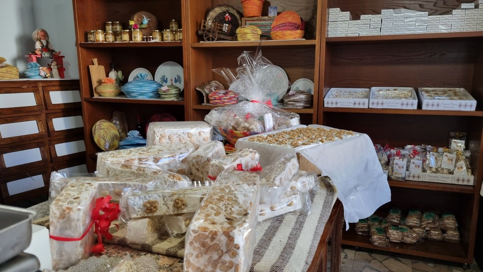Espositore da negozio con torrone confezionato e scaffali decorativi con articoli vari.