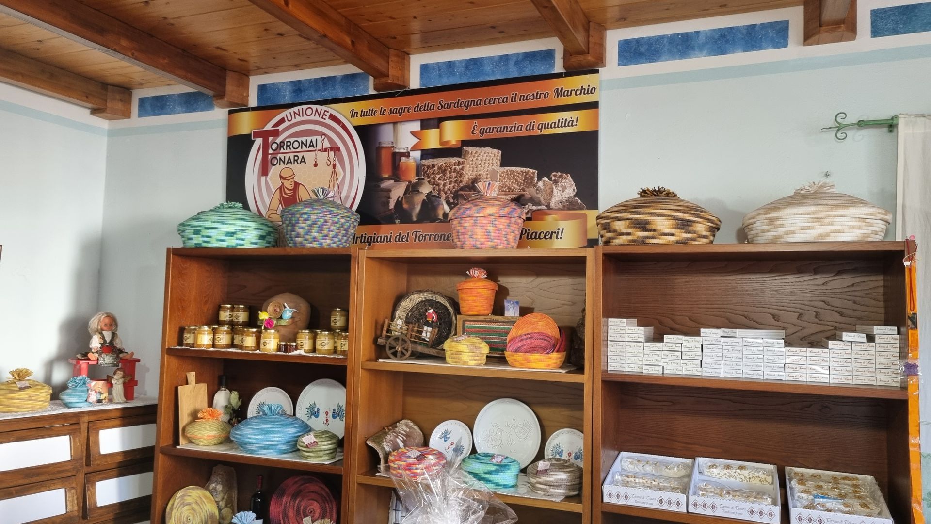 Scaffali in legno espongono oggetti artigianali, tra cui cesti e ceramiche, in un negozio con un'insegna.