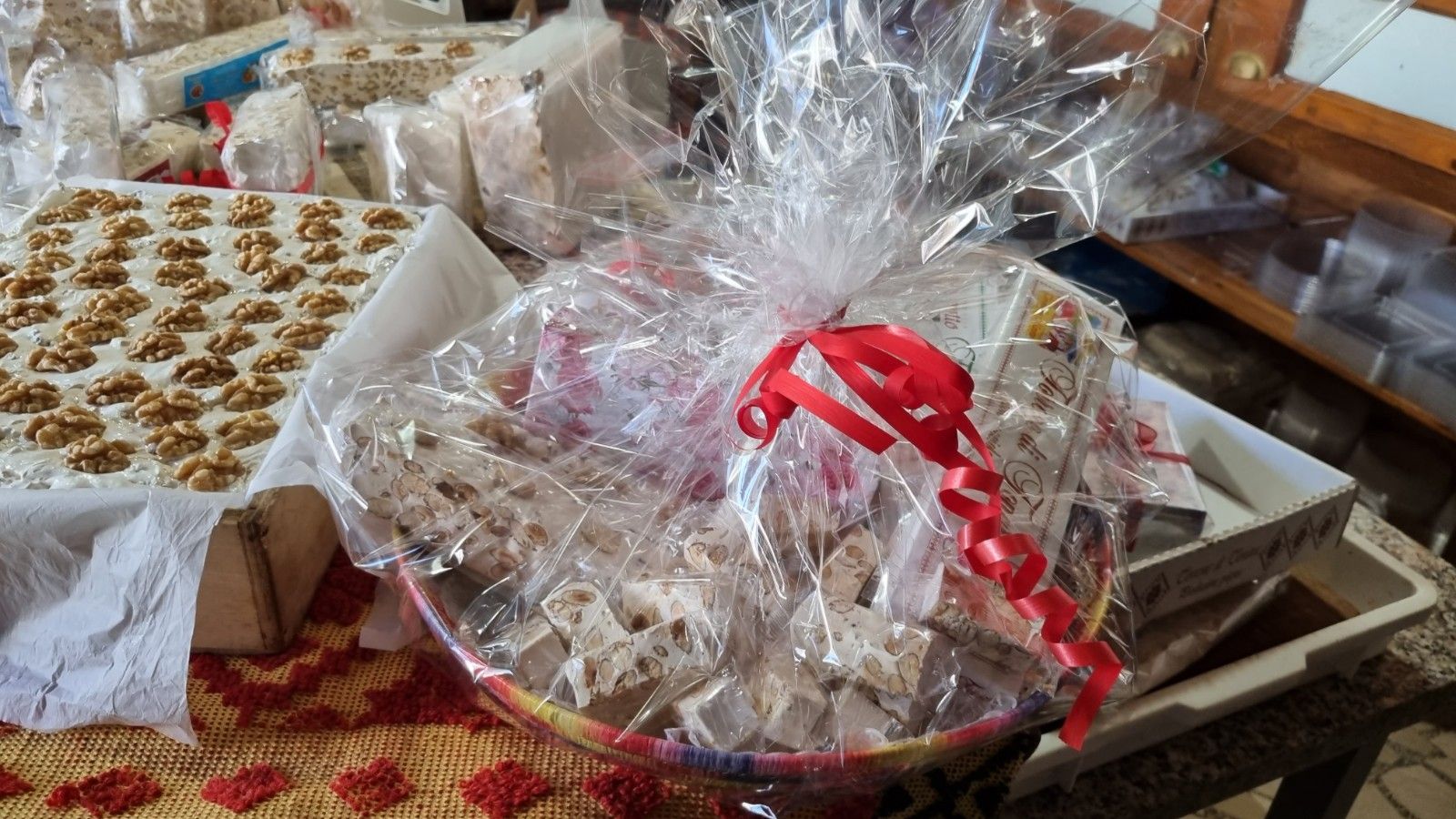 Cesto regalo di torrone legato con un nastro rosso, insieme a un vassoio di dolci ricoperti di noci.