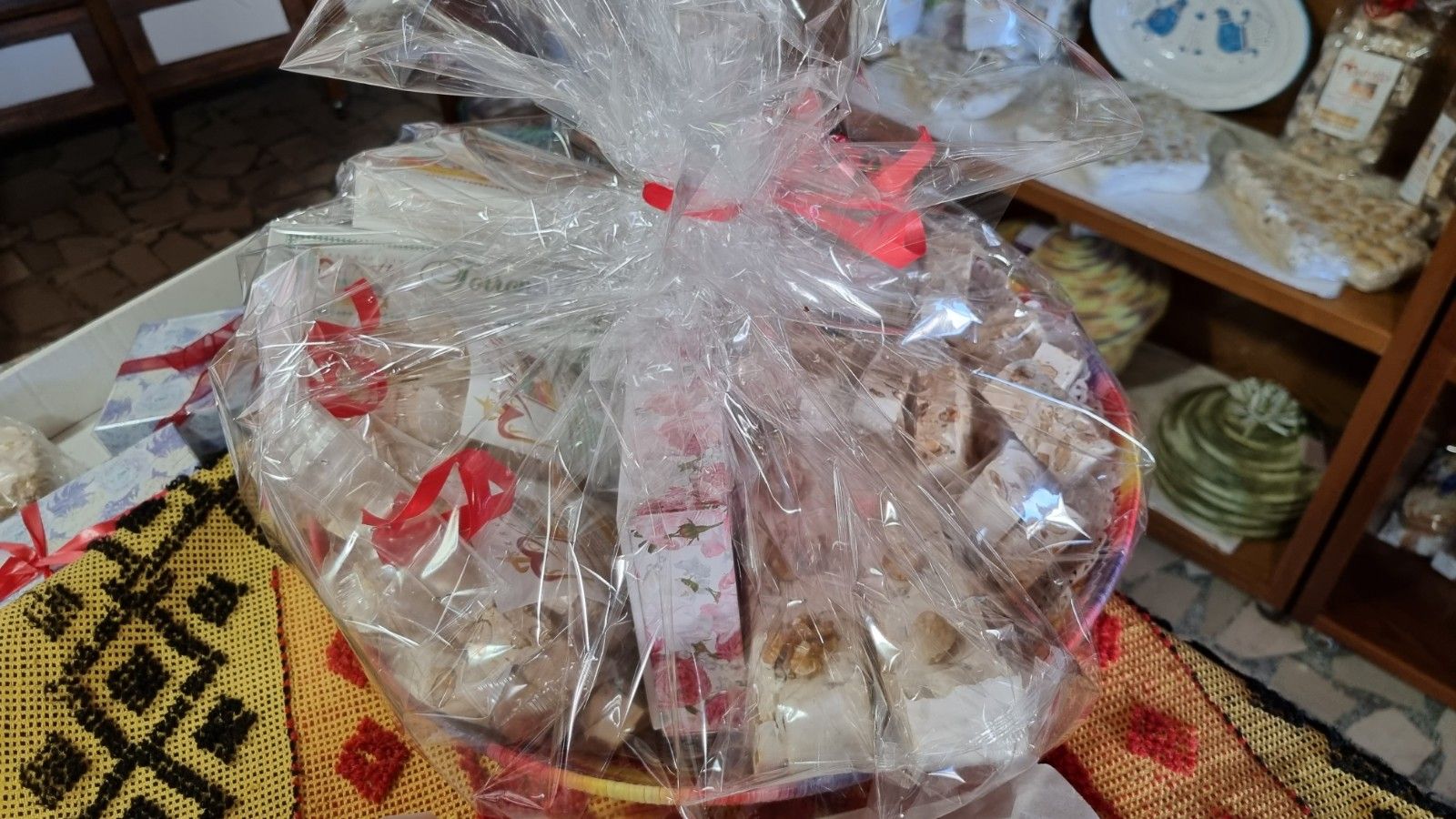 Cesto regalo di torrone assortito, avvolto in cellophane e legato con nastri rossi.