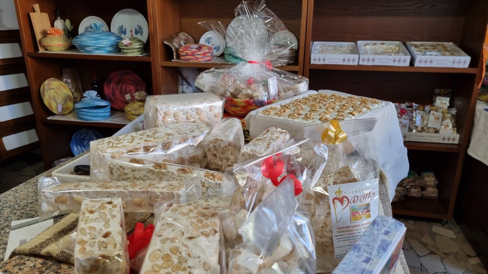 Esposizione di dolci al torrone confezionati in un negozio, con scaffali di oggetti decorativi sullo sfondo.