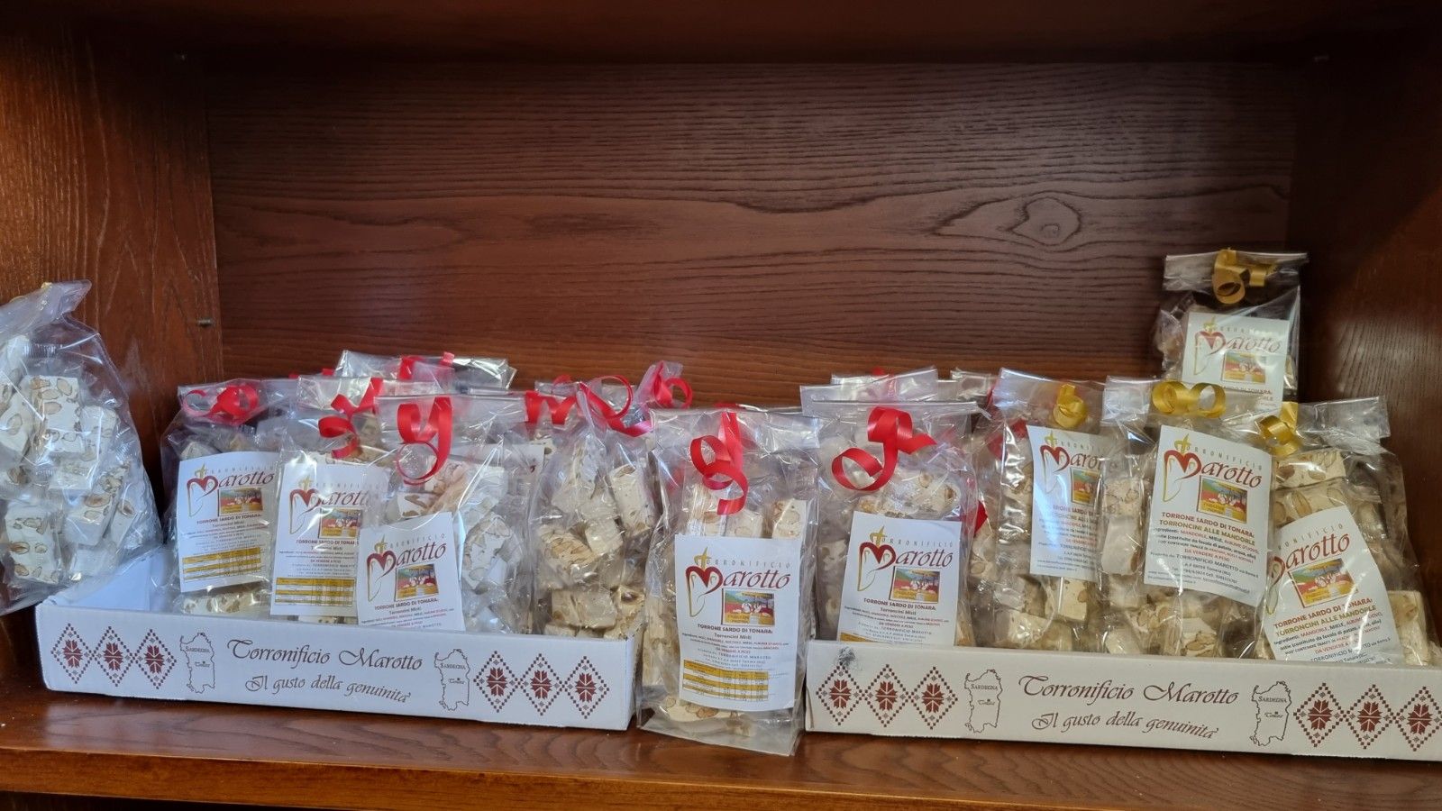 Scaffali che espongono sacchetti trasparenti di torrone bianco con nastri rossi e un'etichetta con un logo.