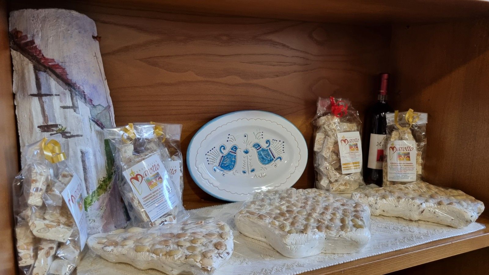 Esposizione di torrone, piatto e vino su uno scaffale di legno.