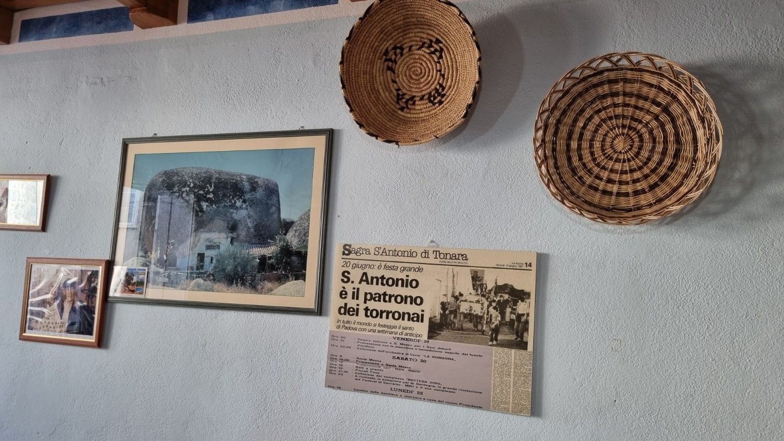 Parete con quadri incorniciati, ritagli di giornale e cestini intrecciati.
