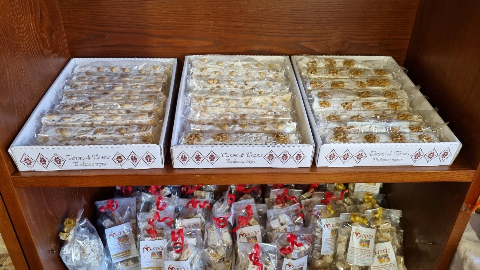 Scatole di torrone con noci su uno scaffale di un negozio, sotto dolciumi confezionati.