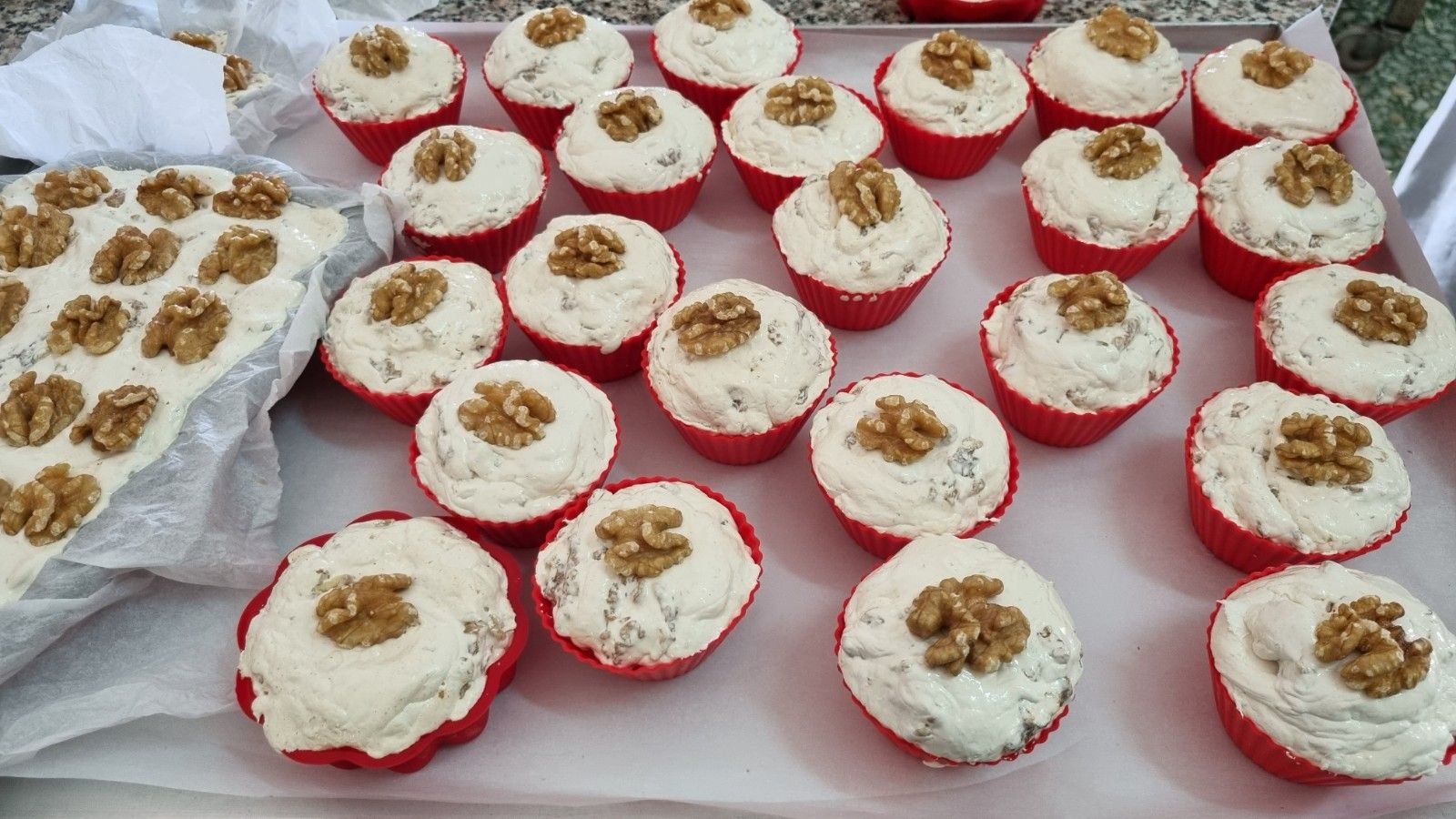 Vassoio di cupcakes ricoperti di glassa bianca e noci, in pirottini rossi.