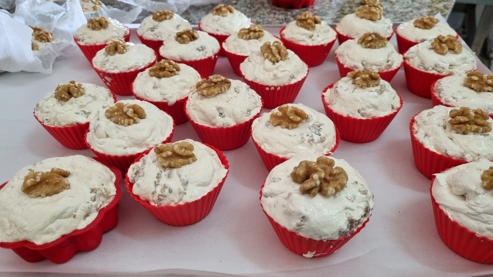 Pirottini rossi per cupcake riempiti con cupcake glassati di bianco e decorati con metà noci.